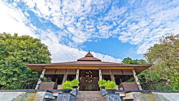 A traditional pavilion with a tiled roof, surrounded by greenery and a clear sky.