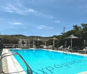 Una piscina al aire libre, sombrillas, sillones reclinables de piscina