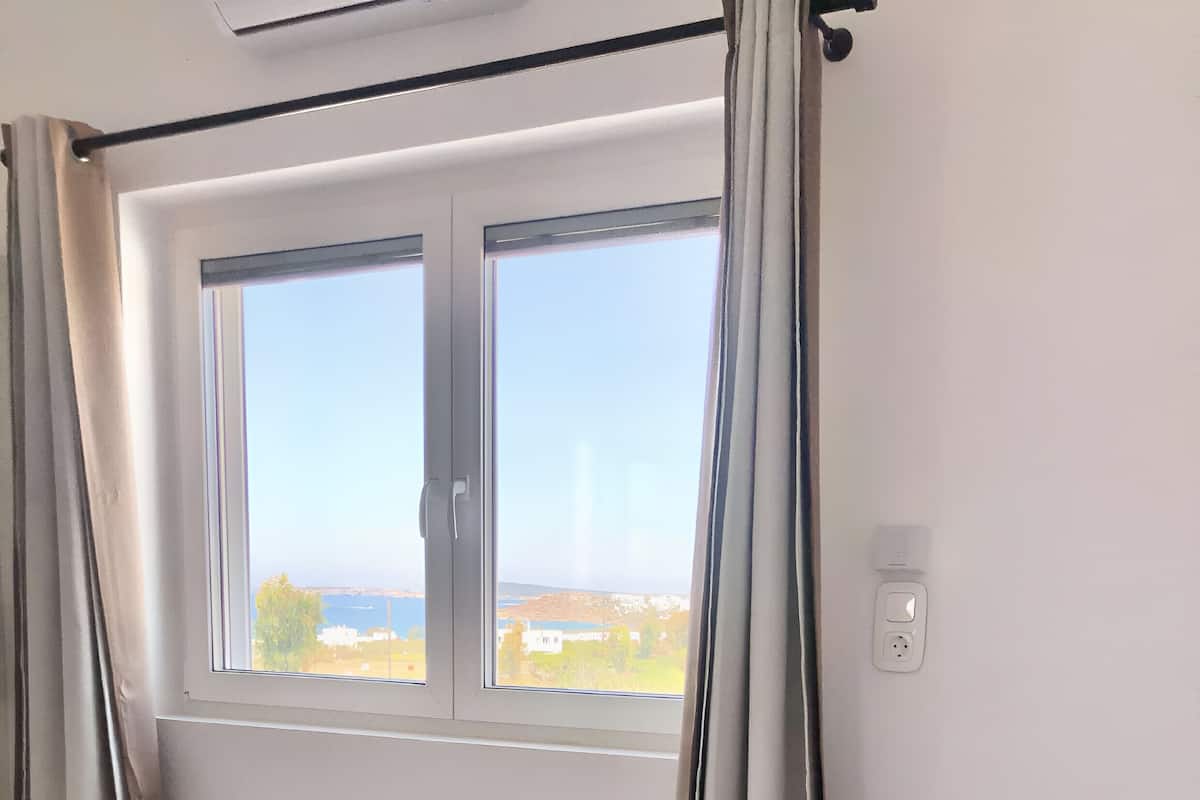 A hotel room with a bed, a window with curtains, and a view of the outdoors.