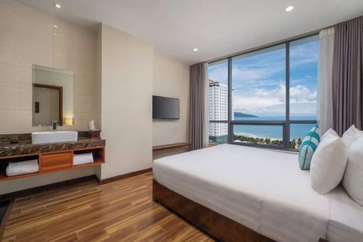 A hotel room with a large bed, a bathroom with a mirror and sink, and a view of a cityscape.