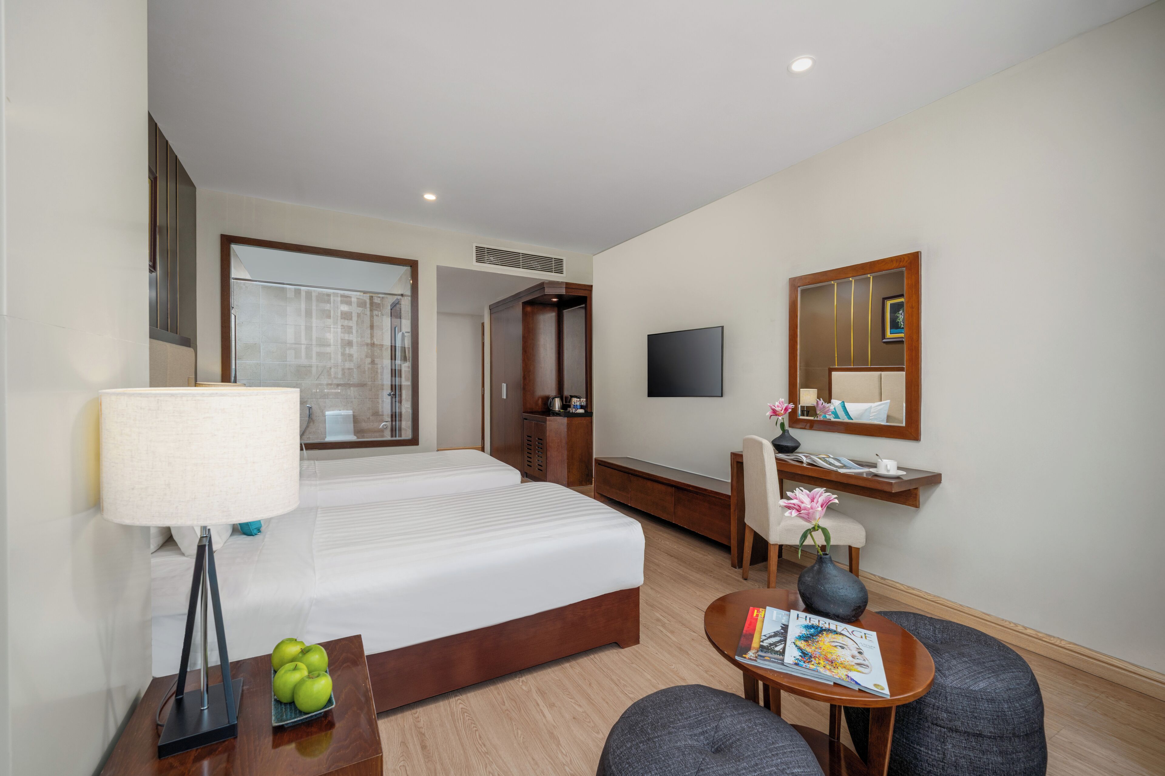 A hotel room with a bed, a desk, a chair, a TV, a mirror, and a small table with a magazine.