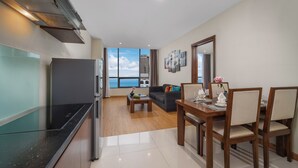 A modern living room with a dining area, kitchen, and large windows offering a view of the city skyline. - Avatar Danang (Da Nang)