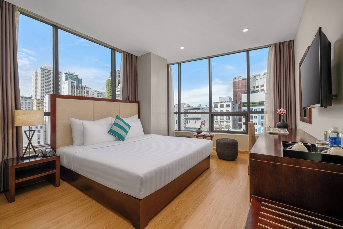 A hotel room with a large bed, a desk, a TV, and a view of the cityscape.