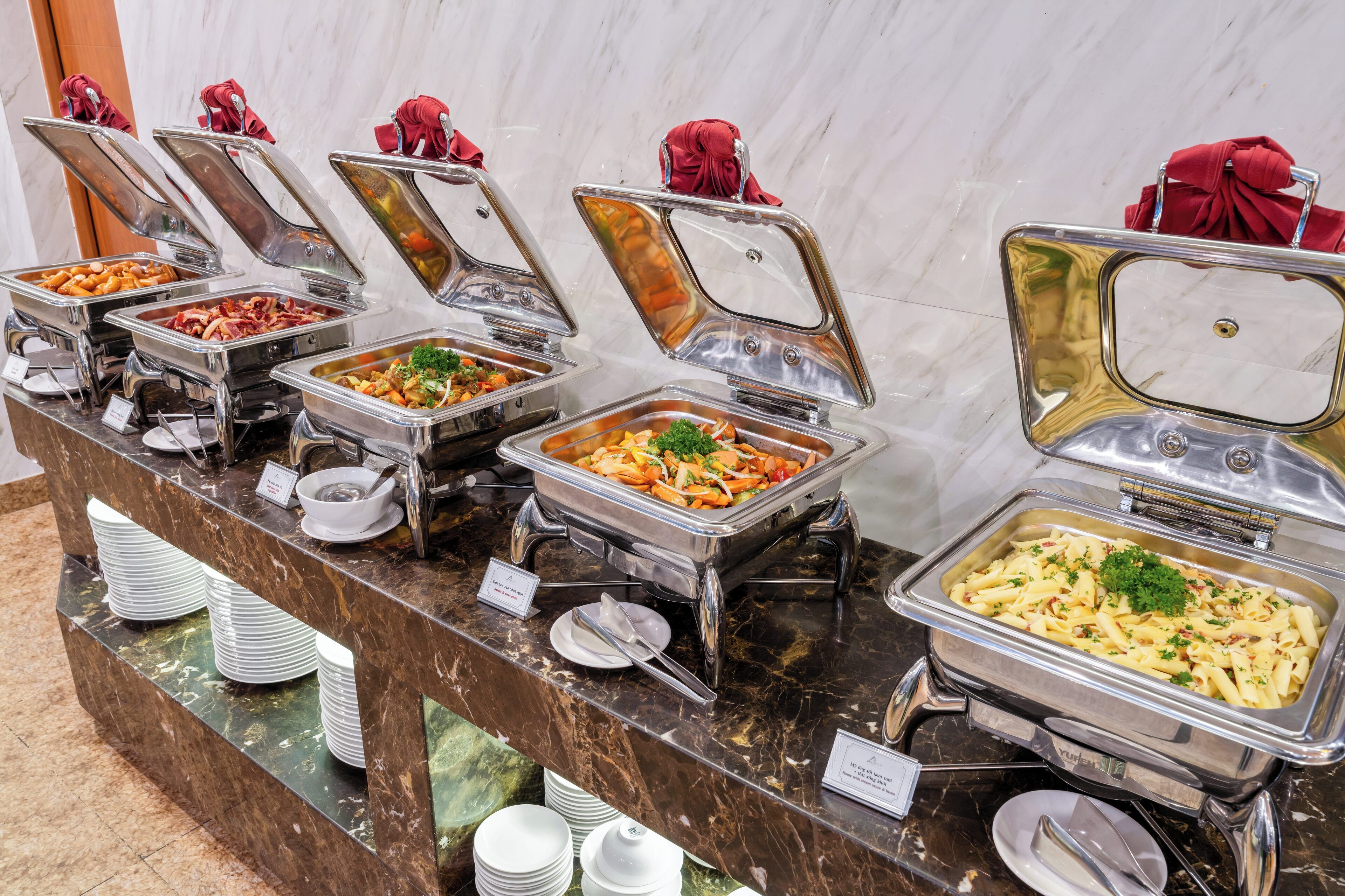 Un buffet proposant une variété de plats, avec différents postes de service, chacun équipé d’un plateau de service en métal et d’un porte-serviettes rouge.