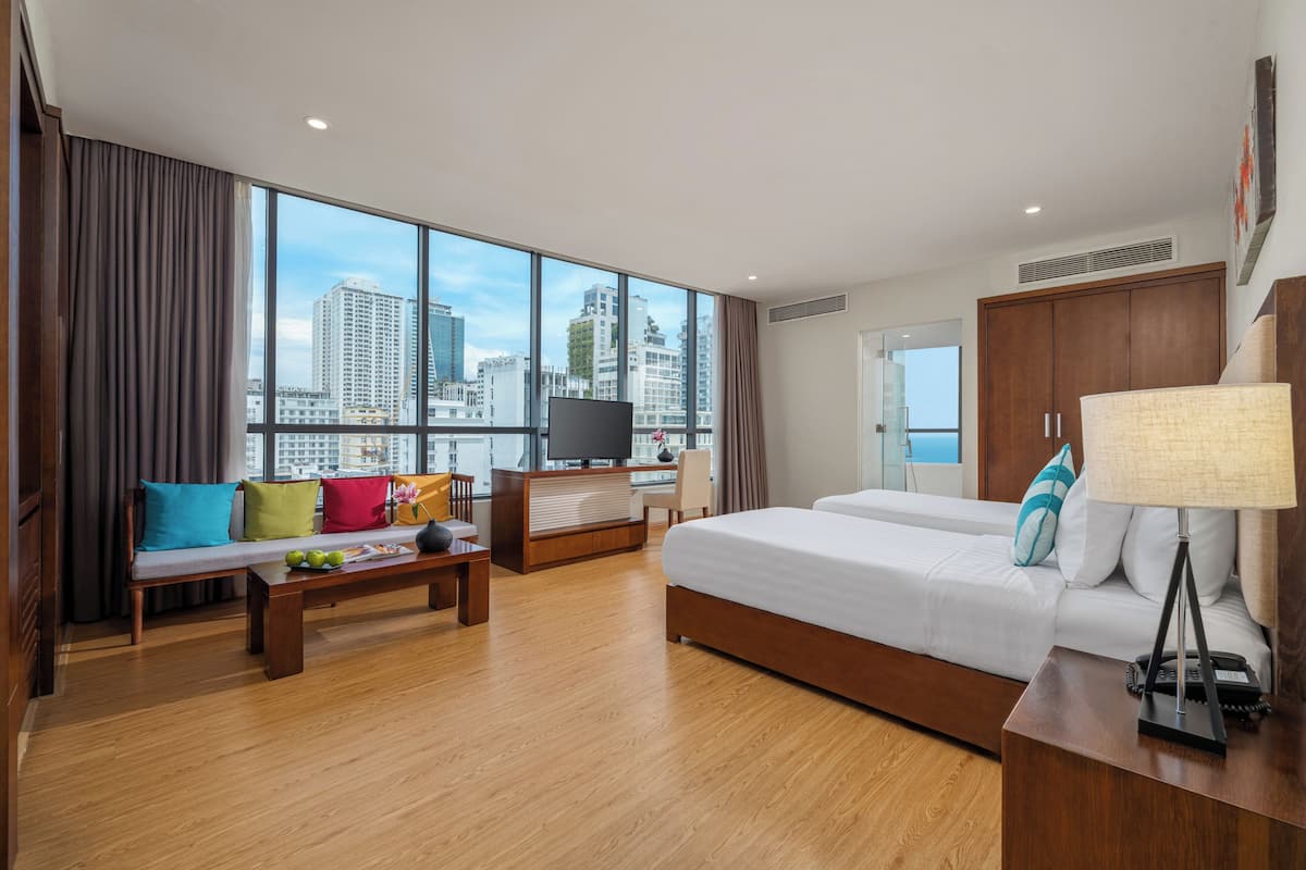 A modern hotel room with a large window, a bed, a desk, and a seating area.