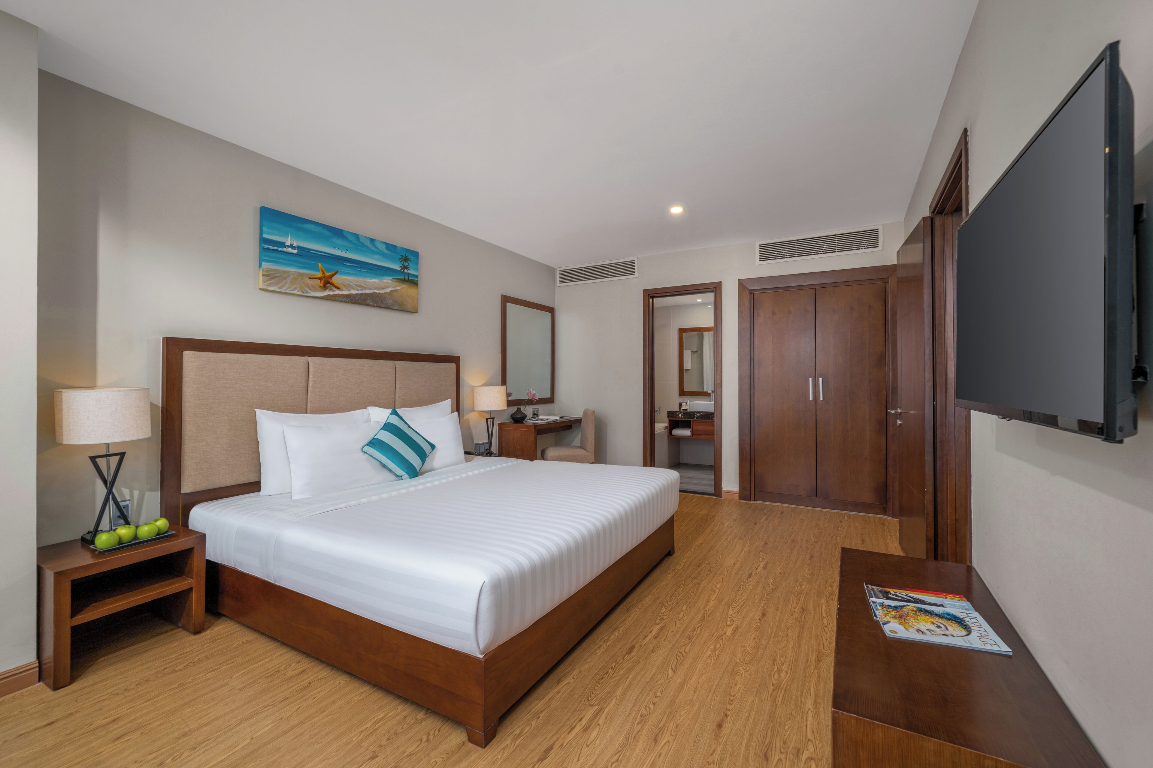 Habitación de hotel con una cama grande, mesitas de noche, un escritorio, un espejo, un televisor y un cuadro en la pared.