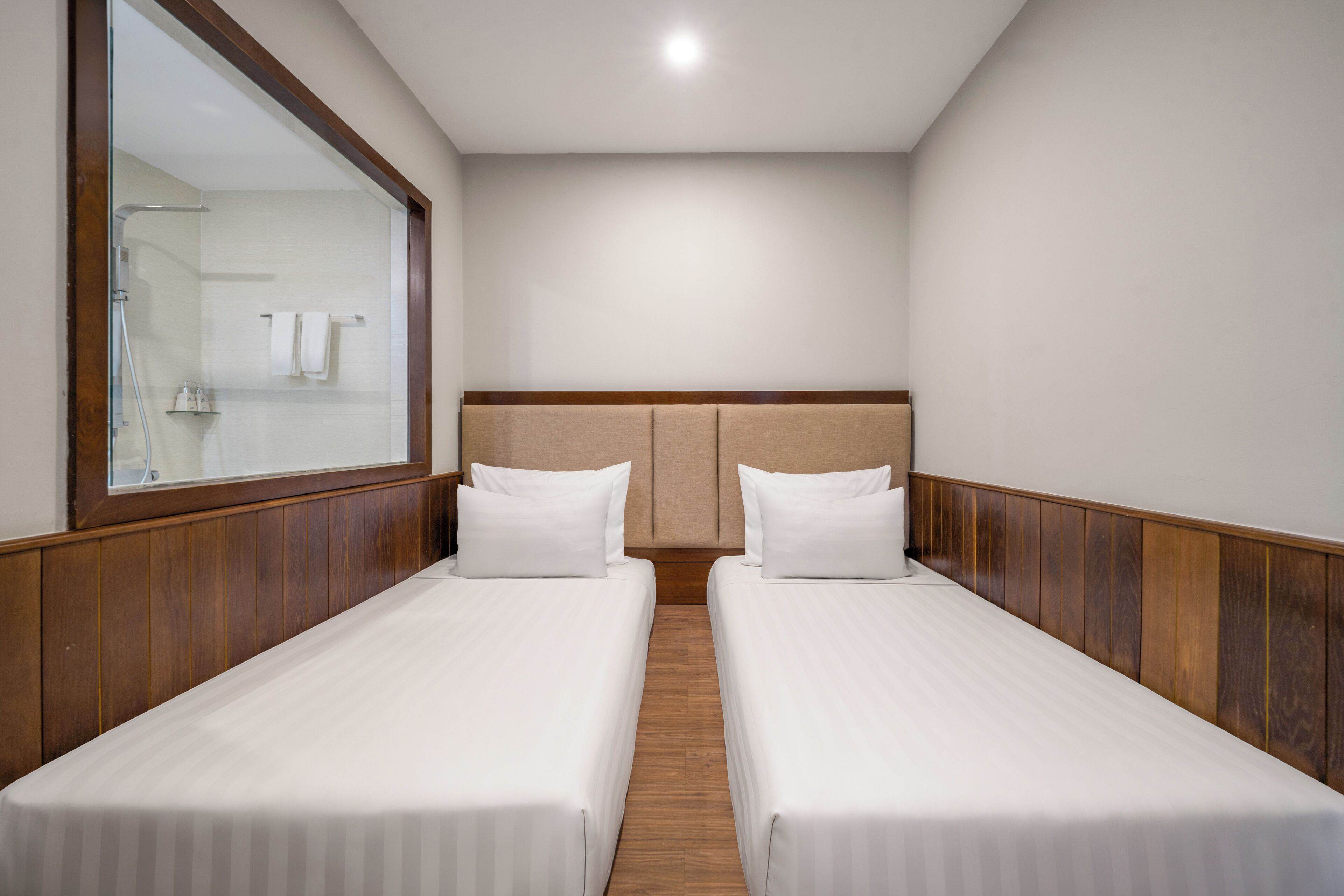 Habitación de hotel con dos camas individuales, paneles de madera en las paredes, un espejo grande y cabecero de madera.