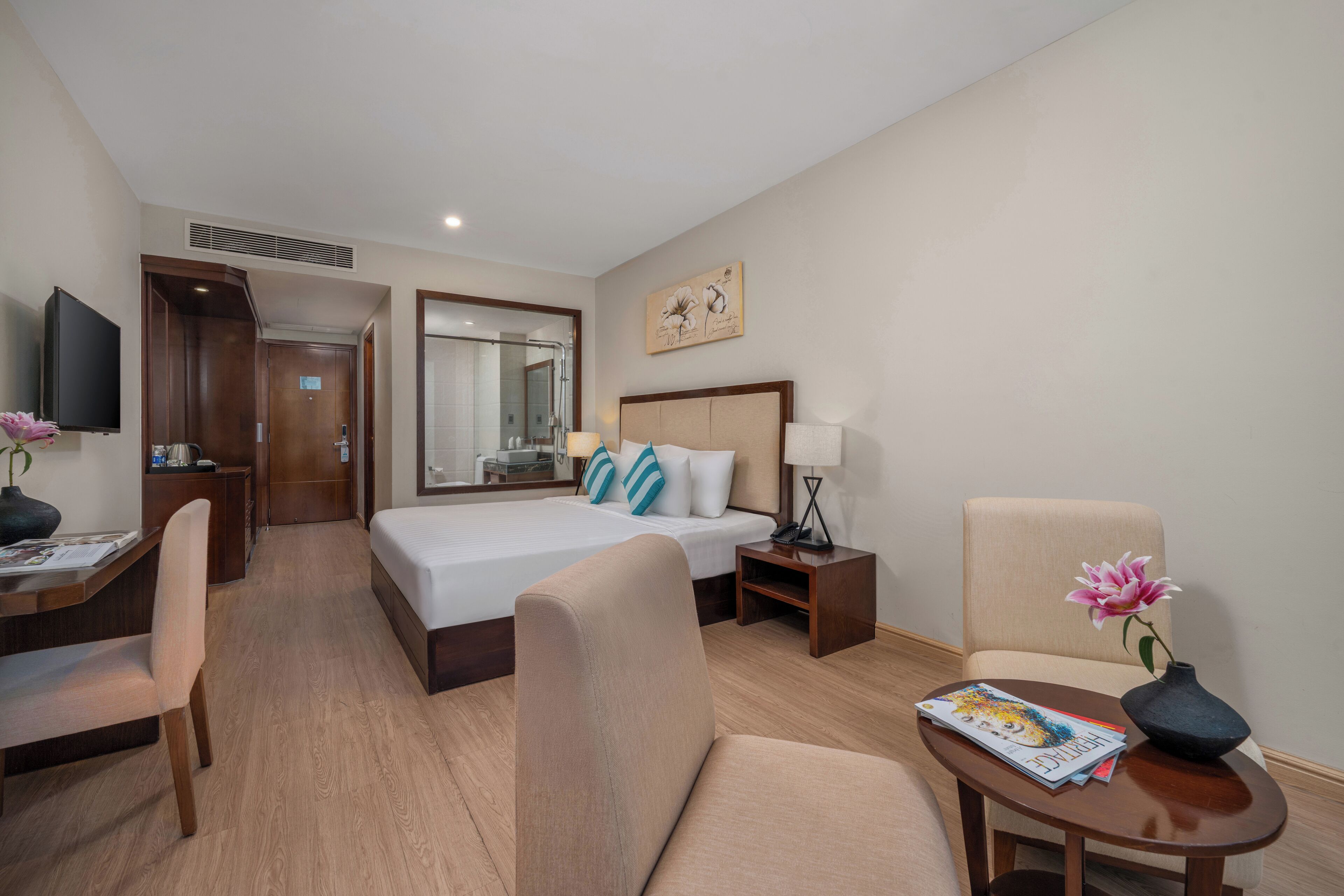 A hotel room with a bed, a desk, a chair, a small table, and a TV.
