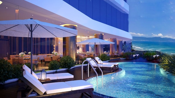 A poolside area with lounge chairs and umbrellas, a dining setup, and a view of the ocean. - Avatar Danang (Da Nang)