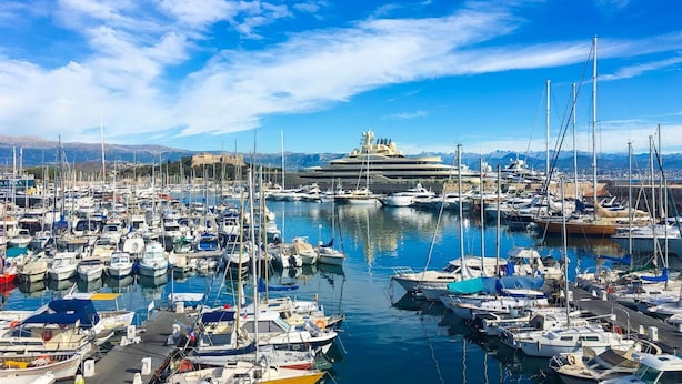 Un port de plaisance rempli de bateaux et de yachts de toutes sortes, avec un grand navire de croisière amarré au loin.