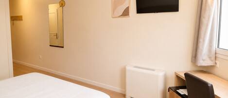 A hotel room with a bed, a desk, a chair, a radiator, a TV, and a mirror.