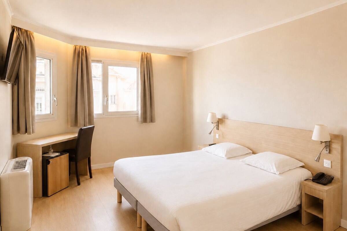 A hotel room with a bed, bedside tables, a desk with a chair, and a window with curtains.