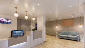 Un espace d’accueil au design moderne, comprenant un comptoir de réception, un téléviseur à écran plat et un canapé bleu clair.