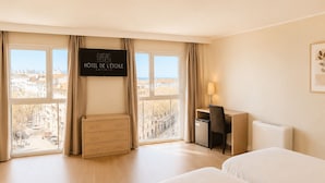 Une chambre d’hôtel avec deux lits, un bureau, une commode et un téléviseur affichant le texte « HÔTEL DE LÉTOILE ANTIBES ».
