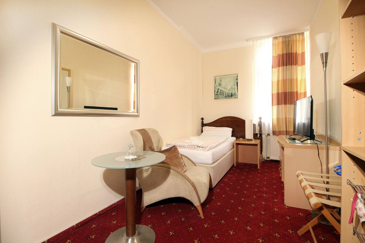 Une chambre d’hôtel équipée d’un lit, d’un bureau, d’une chaise, d’une table, d’un miroir et d’un téléviseur.