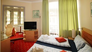 A hotel room with a bed, a desk with a TV, a chair, and a window with curtains. - Hotel Neustädter Hof (Titisee-Neustadt)