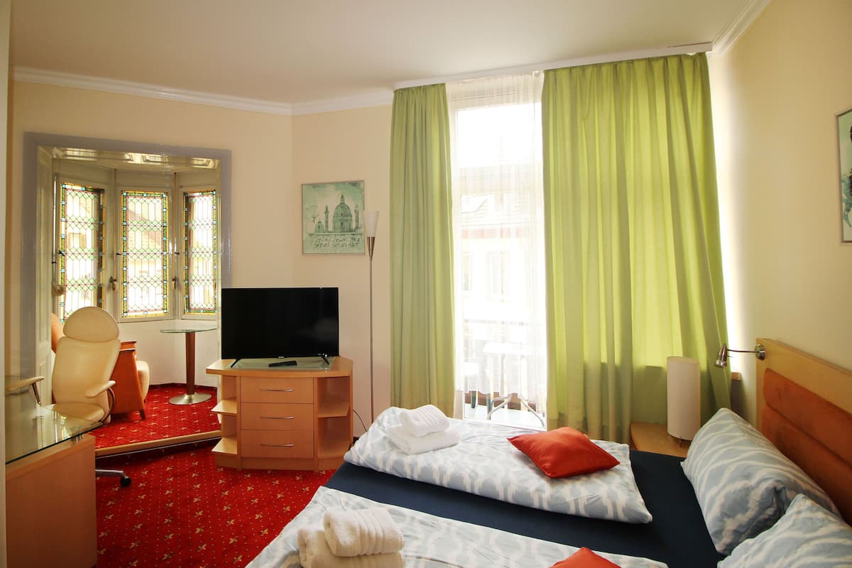Une chambre d’hôtel avec un lit, un bureau avec une télévision, une chaise et une fenêtre avec des rideaux.