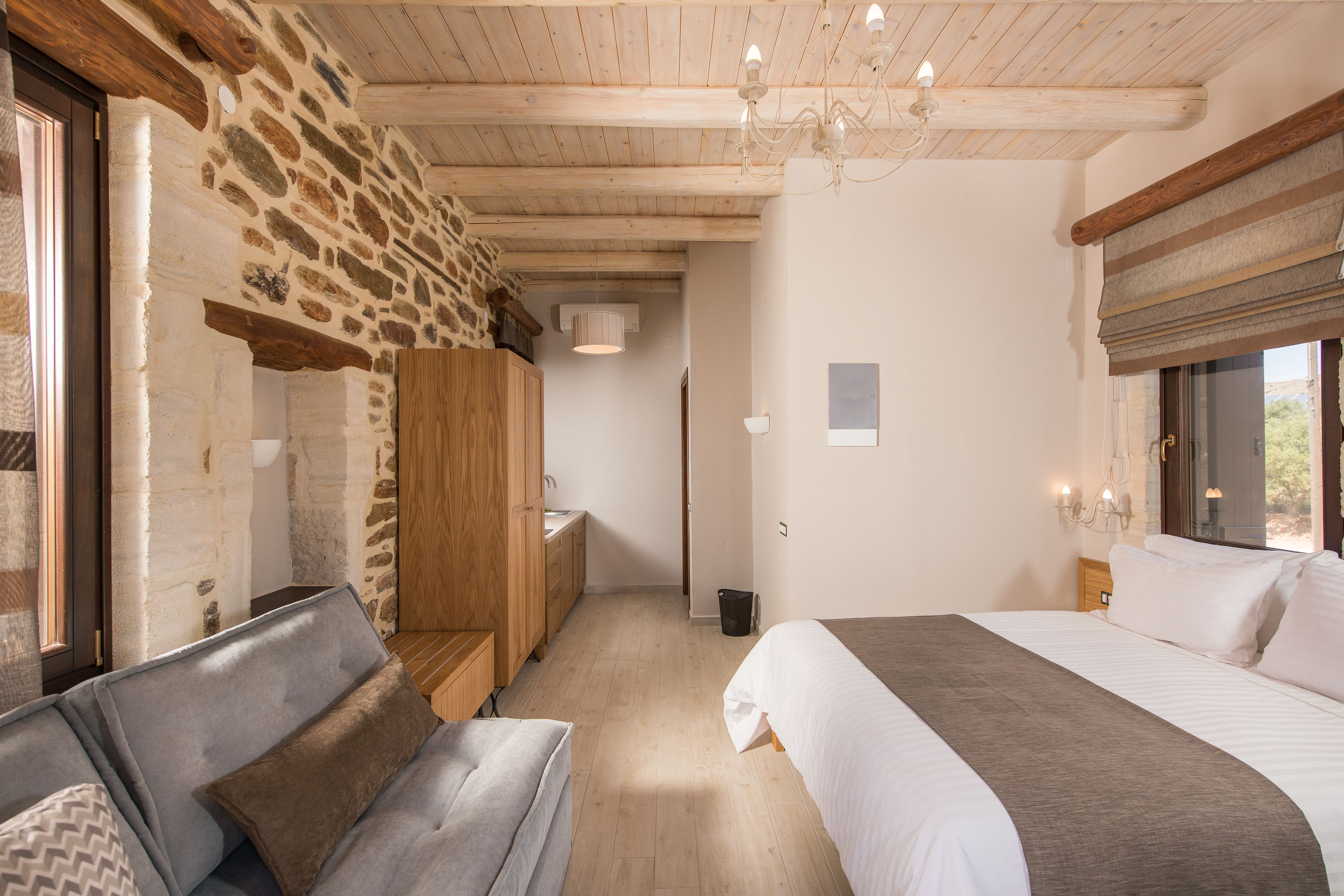 A bedroom with a large bed, a wooden wardrobe, a sofa, and a stone wall.