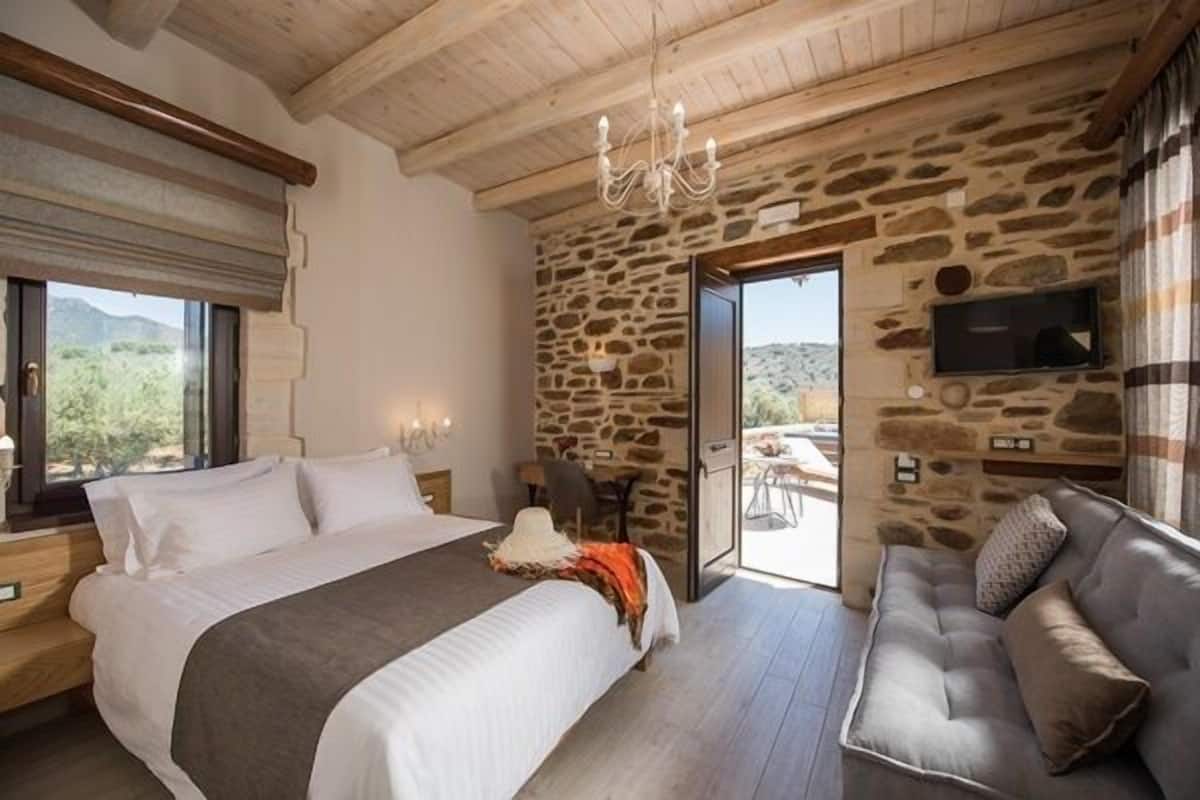 Een slaapkamer met een groot bed, een bank, een stenen muur en een televisie.