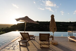 Una piscina infinita con sillones y sombrillas, con vistas a un paisaje montañoso.