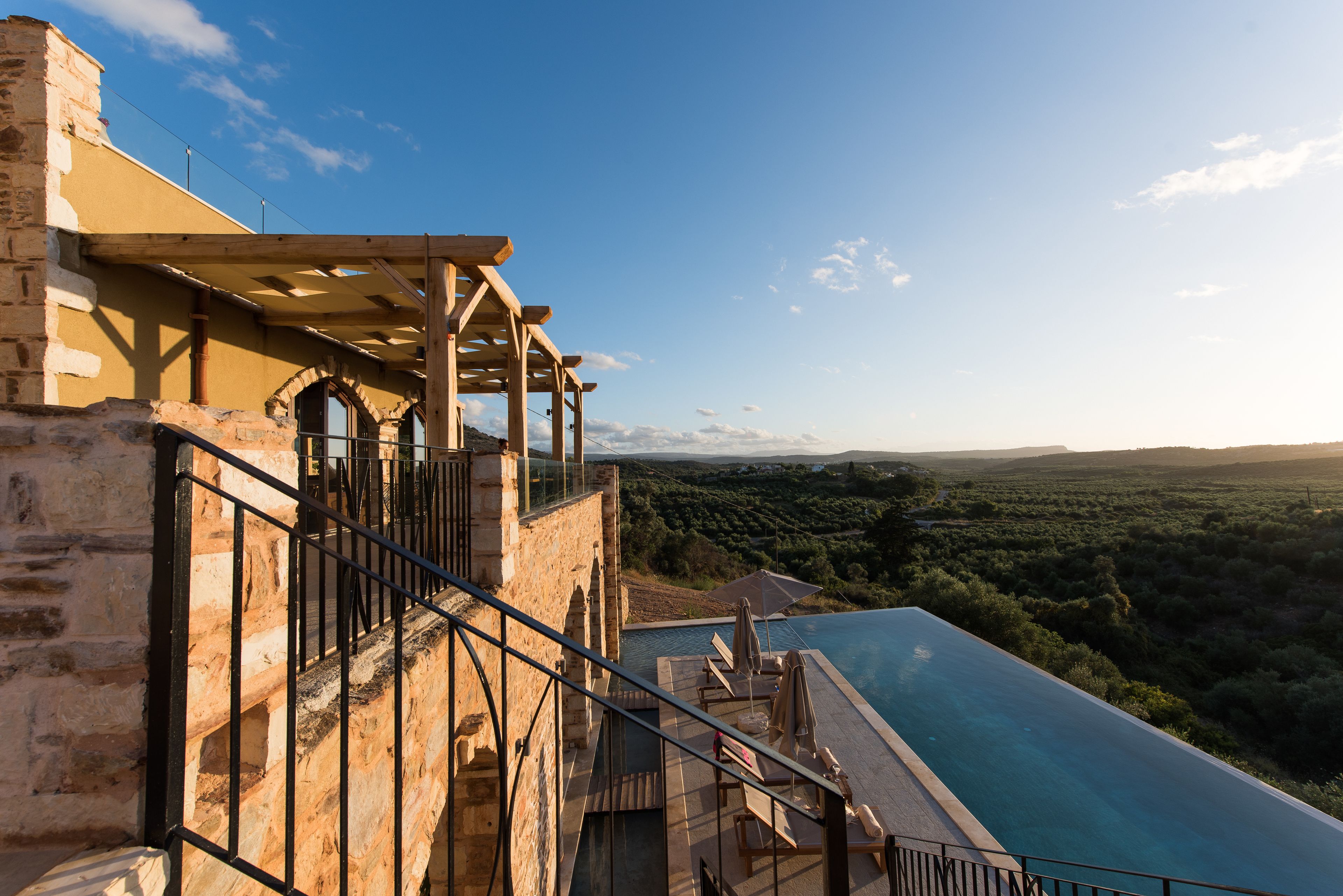 Edificio de piedra con balcón de madera que da a una piscina y un paisaje pintoresco.