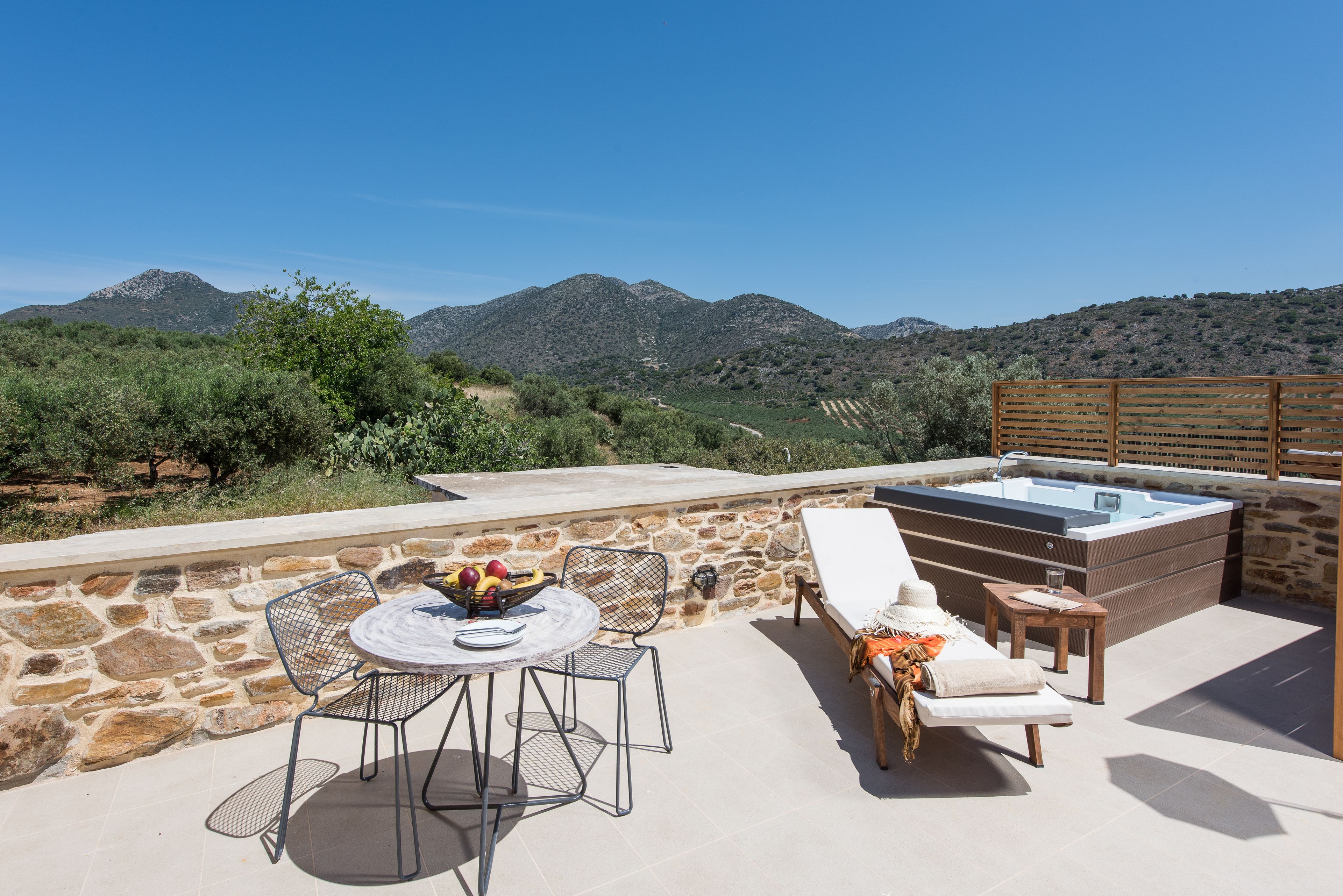 A stone patio with a table, chairs, and a hot tub overlooking a mountainous landscape.