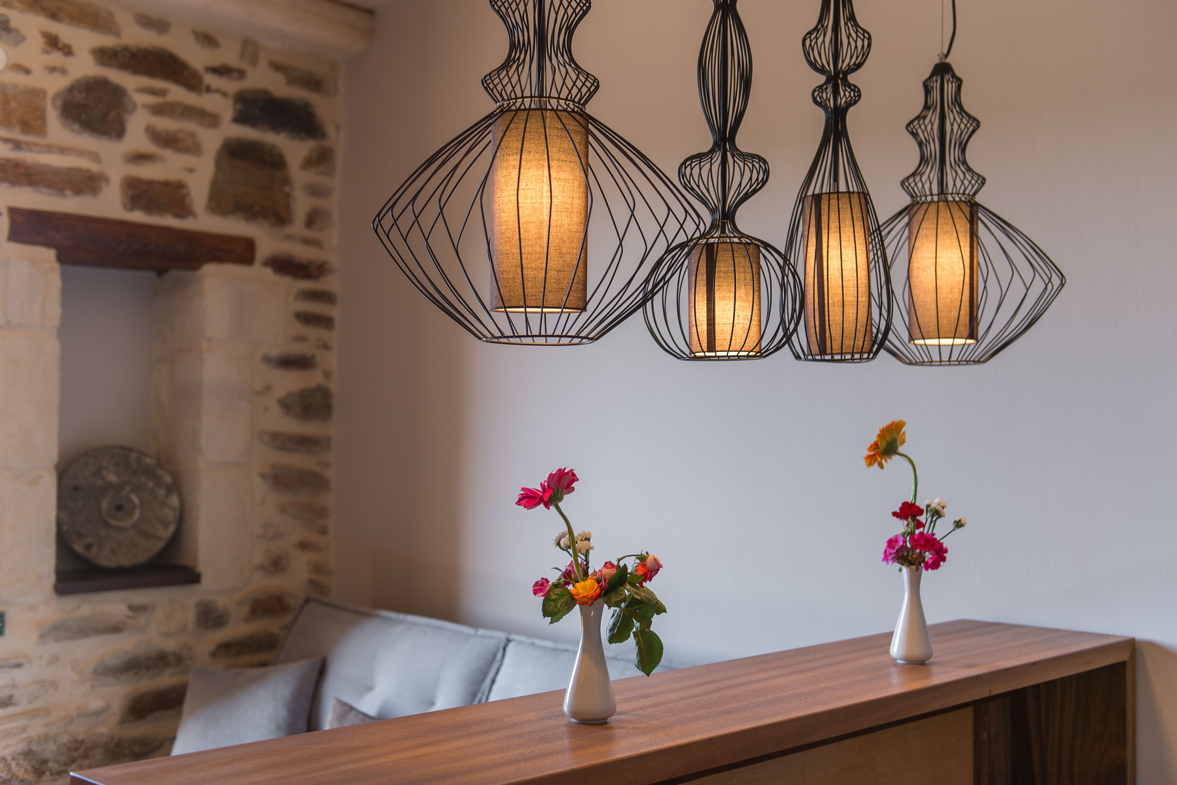 A wooden table with two white vases of flowers, a stone wall, and three hanging pendant lights.