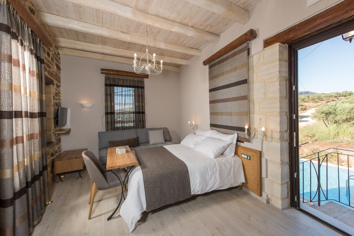 Een slaapkamer met een bed, een bureau, een stoel, een televisie en uitzicht op een zwembad.