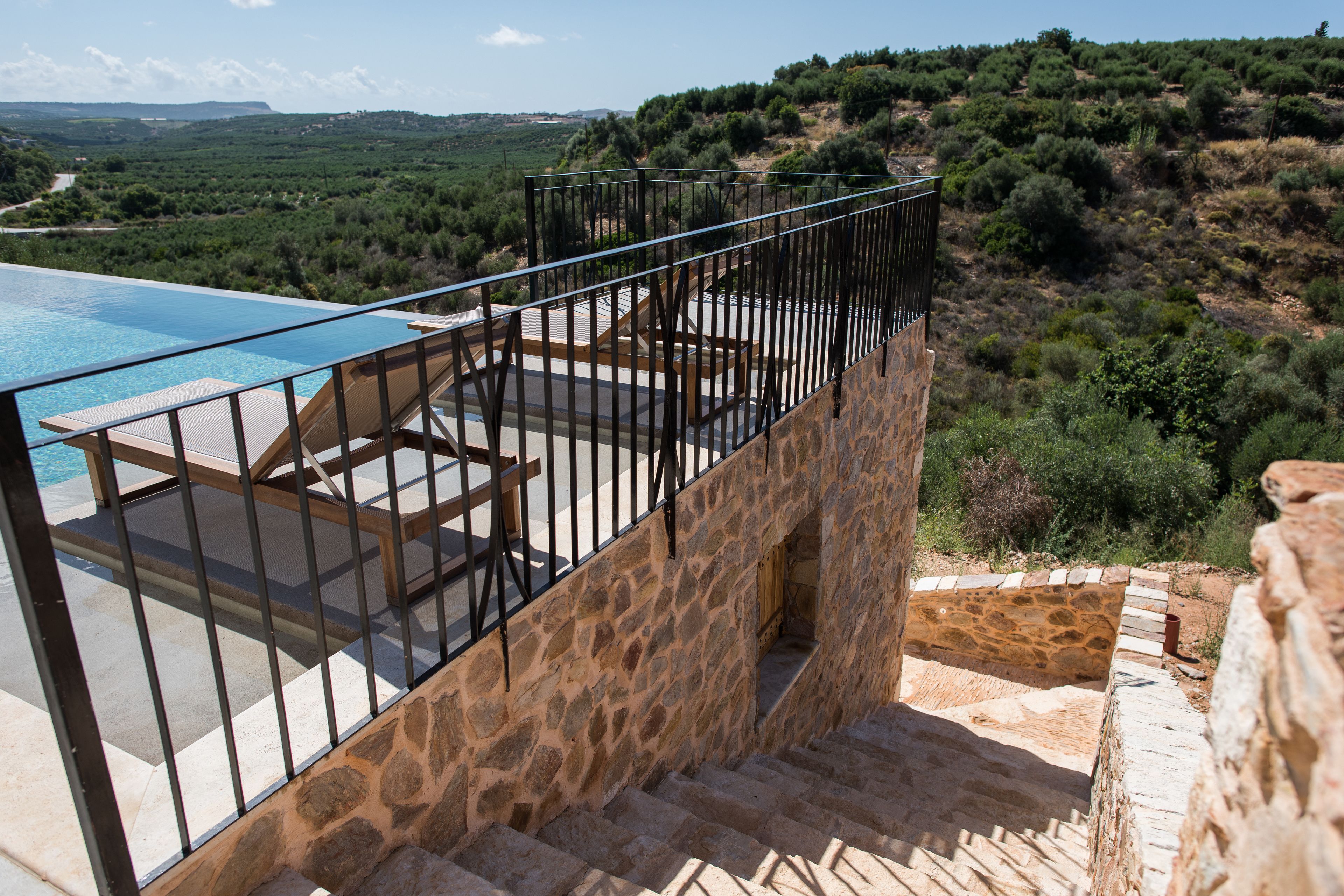 A stone staircase leading to a pool area with a view of a hilly landscape.