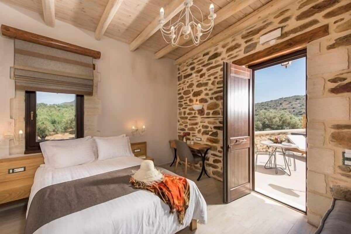 Een slaapkamer met een bed, een kroonluchter, een stenen muur en uitzicht op het buiten.