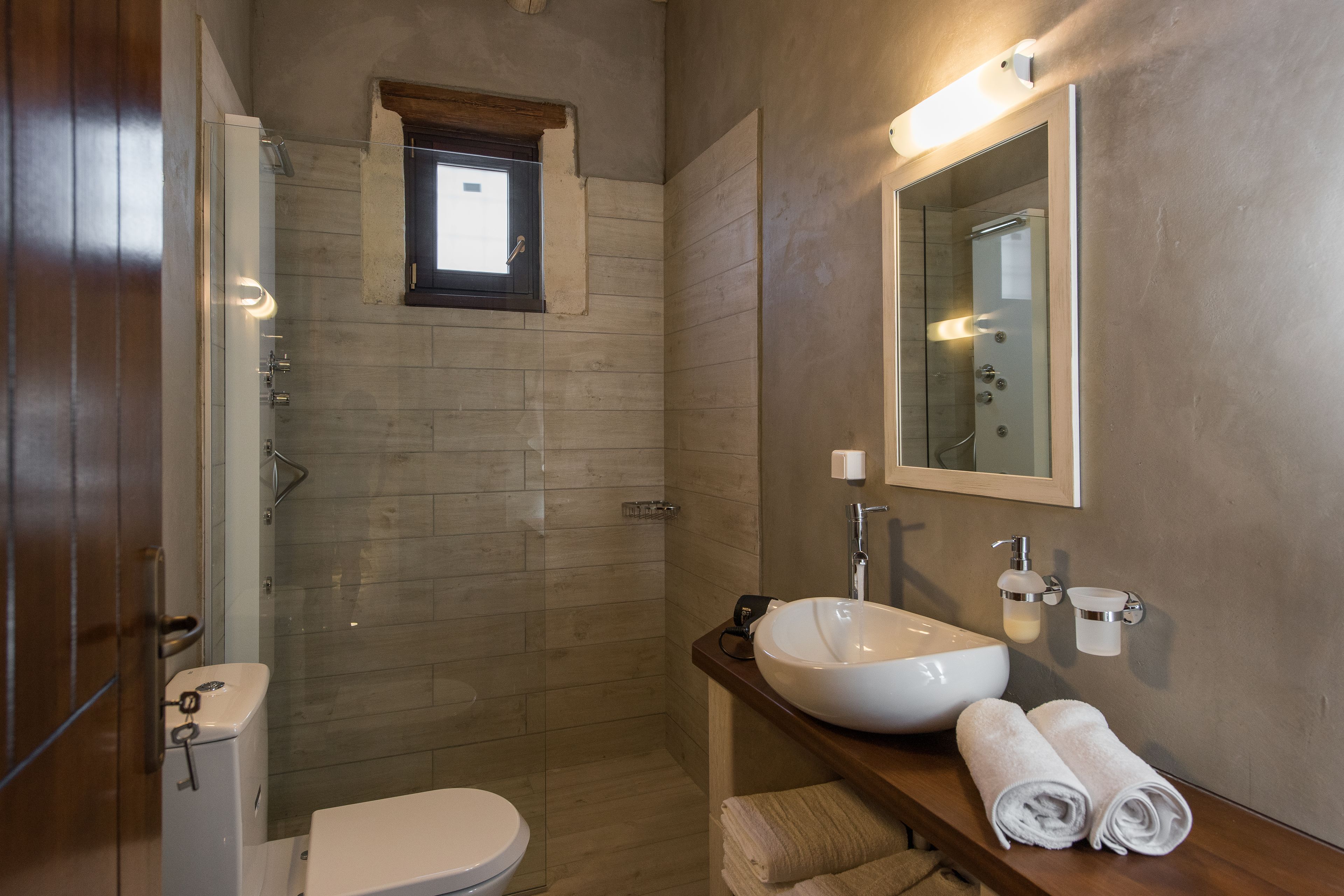 Un baño moderno con ducha envuelta en vidrio, un lavabo blanco y un mueble de tocador de madera.