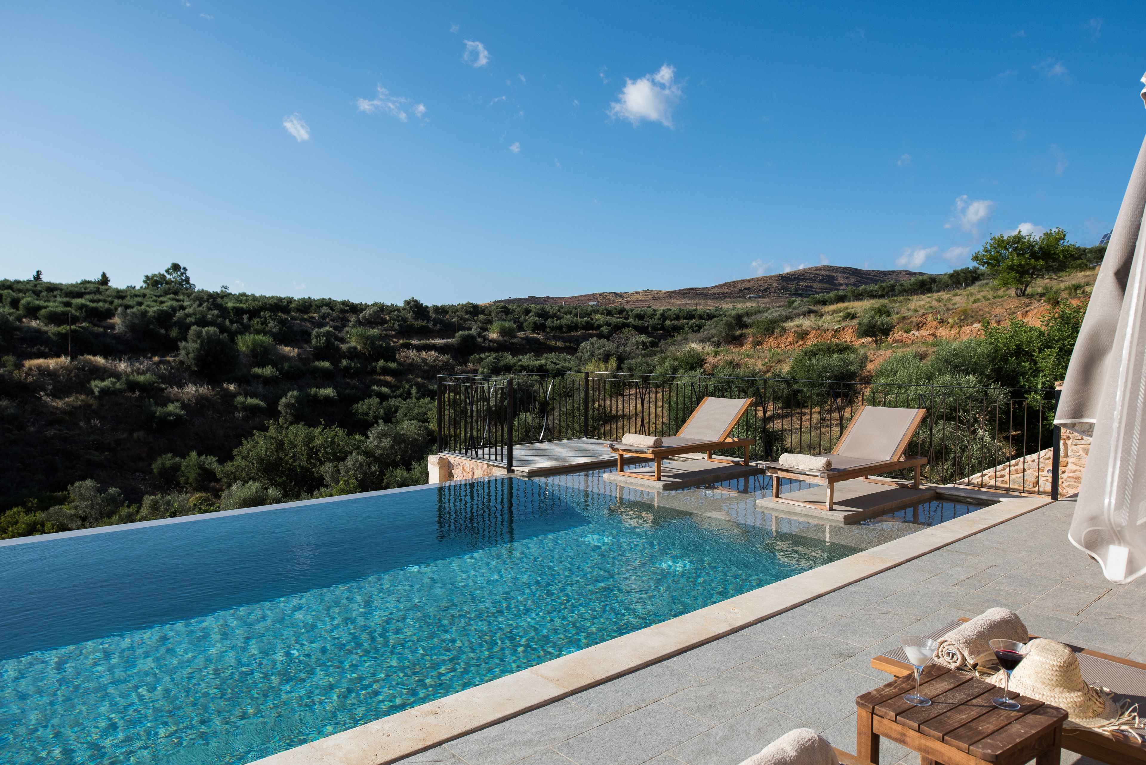 A swimming pool with lounge chairs and a table, surrounded by a landscaped garden and a view of hills.