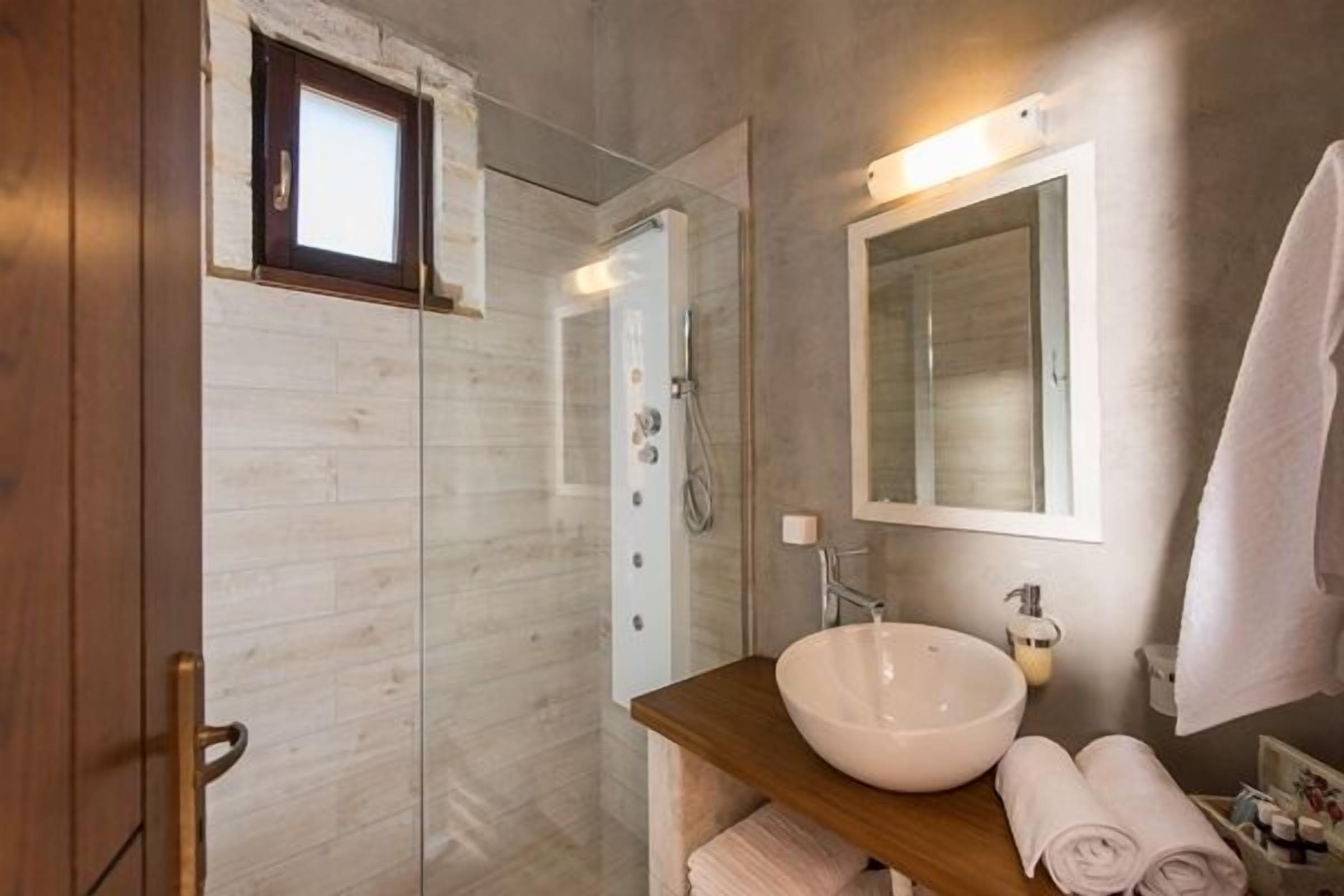 A bathroom with a wooden vanity, a large mirror, a built-in shower, and a small window.