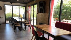 Ein Restaurantinneres mit einem langen Holztisch und Stühlen, großen Fenstern und einer roten Bank.
