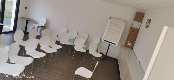 Un salón de conferencias con sillas blancas dispuestas en filas, una pizarra y una pequeña mesa con sillas.