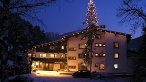 A hotel with a snow-covered ground, a lit Christmas tree, and a car parked in front. - Auderer Hotel (Karroesten)