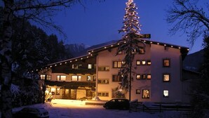 A hotel with a snow-covered ground, a lit Christmas tree, and a car parked in front. - Auderer Hotel (Karroesten)