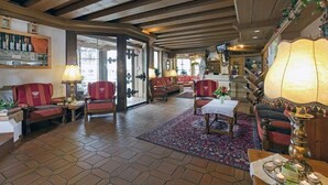 A spacious lobby with wooden beams, red upholstered chairs, a central table, and a staircase leading to upper floors. - Auderer Hotel (Karroesten)
