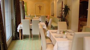 A dining area with tables set for four, white chairs, and a cross on the wall. - Alpenschlössl (Mayrhofen)