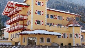 A multi-story building with a distinctive red and white facade, a balcony, and a snow-covered roof, set against a mountainous backdrop. - Alpenschlössl (Mayrhofen)
