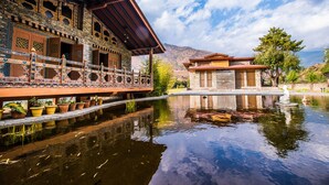 Ein traditionelles Gebäude mit aufwendigen architektonischen Details, einem spiegelnden Wasserspiegel und einer bergigen Kulisse.