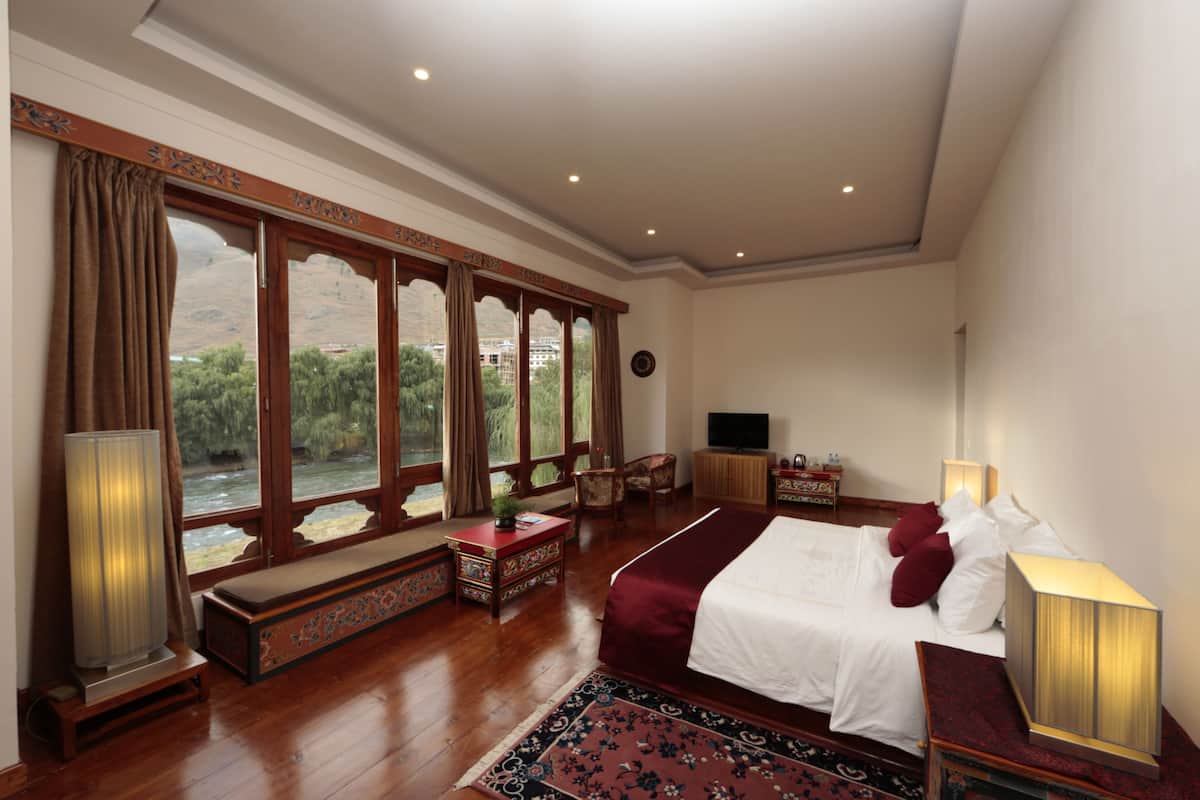 A spacious bedroom with a large bed, a television, and a view of a river through large windows.