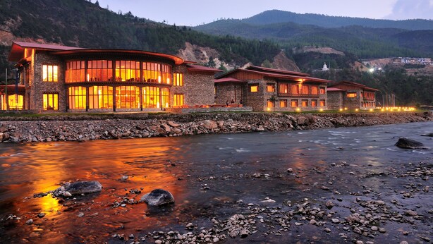 Ein Hotel mit Steinaußenwand und großen Fenstern, gelegen an einem Fluss mit steiniger Uferlinie.