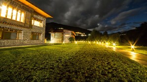 Ein Steinhaus mit großen Fenstern und einem gut beleuchteten Rasen bei Nacht.