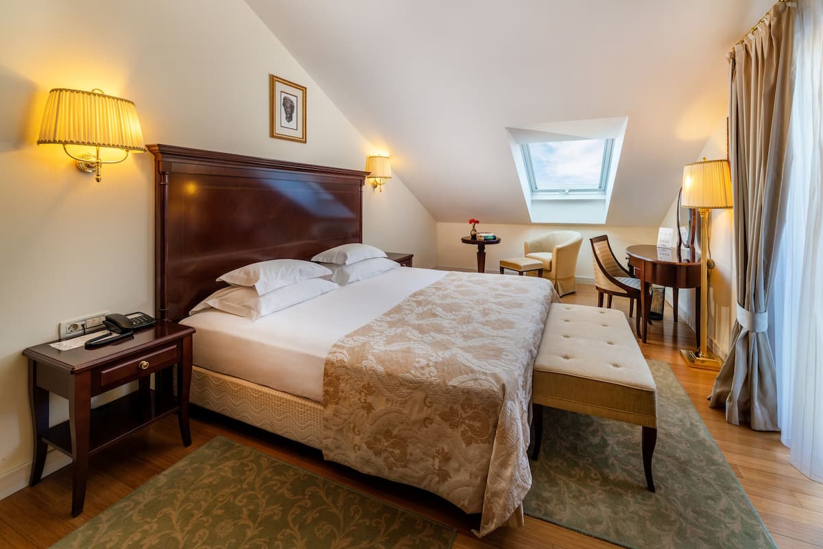 Hotellihuone, jossa on suuri sänky, työpöytä, tuoli ja pieni pöytä, jossa on lamppu.