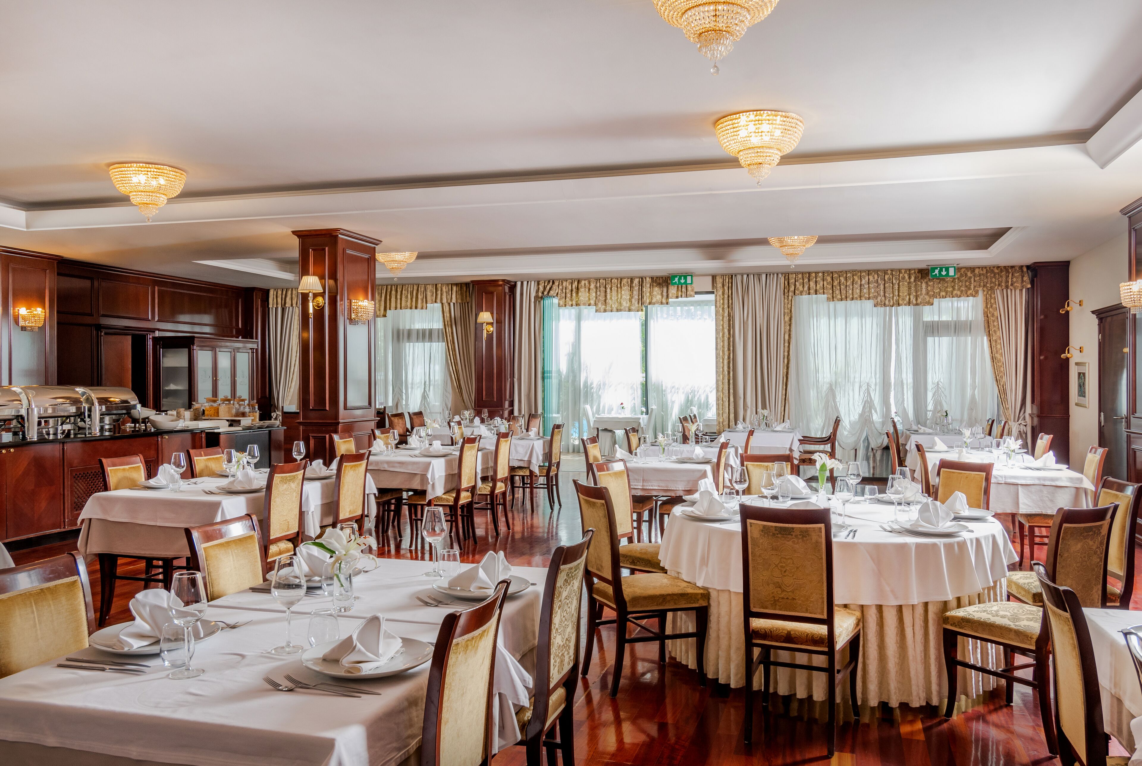 A formal dining room with round tables, chairs, and chandeliers.