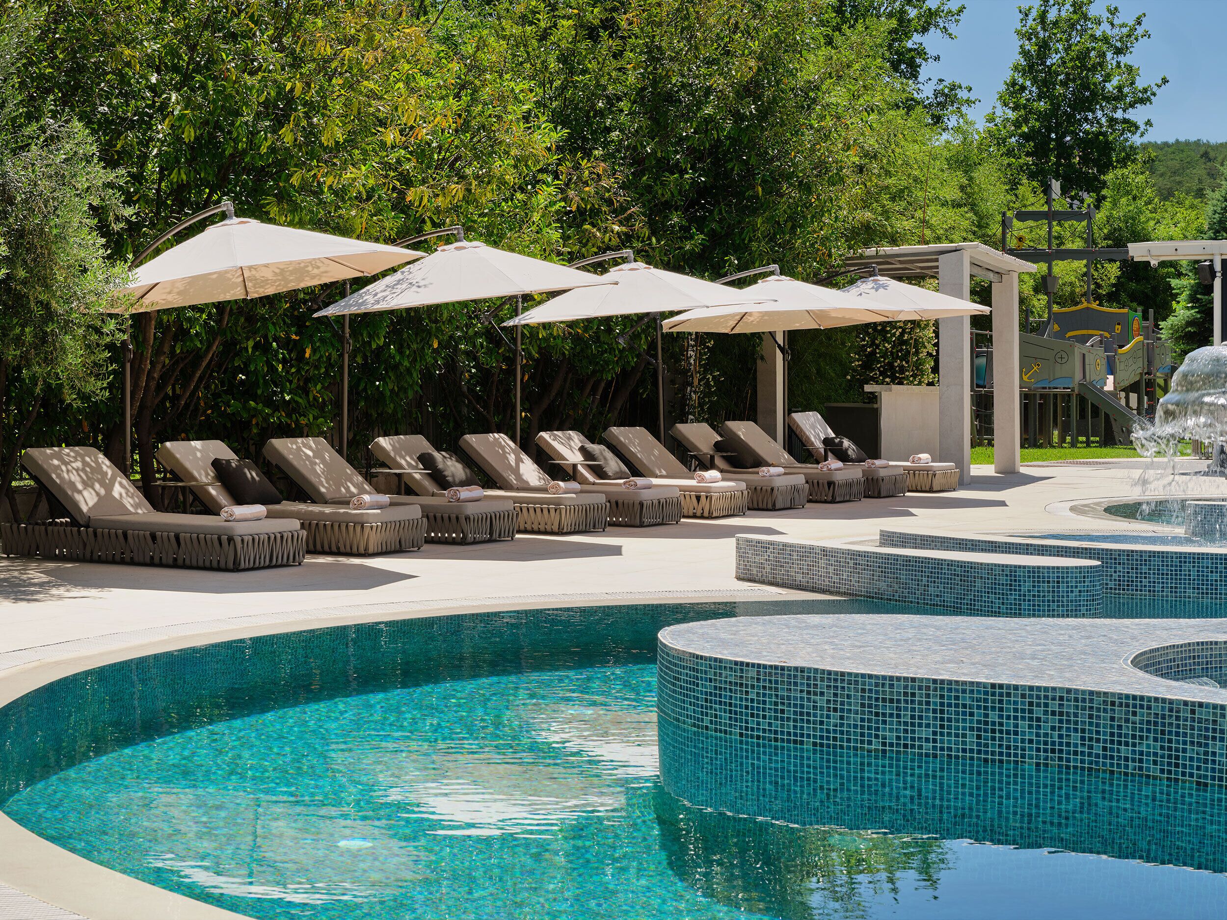 A pool area with lounge chairs and umbrellas, surrounded by greenery.