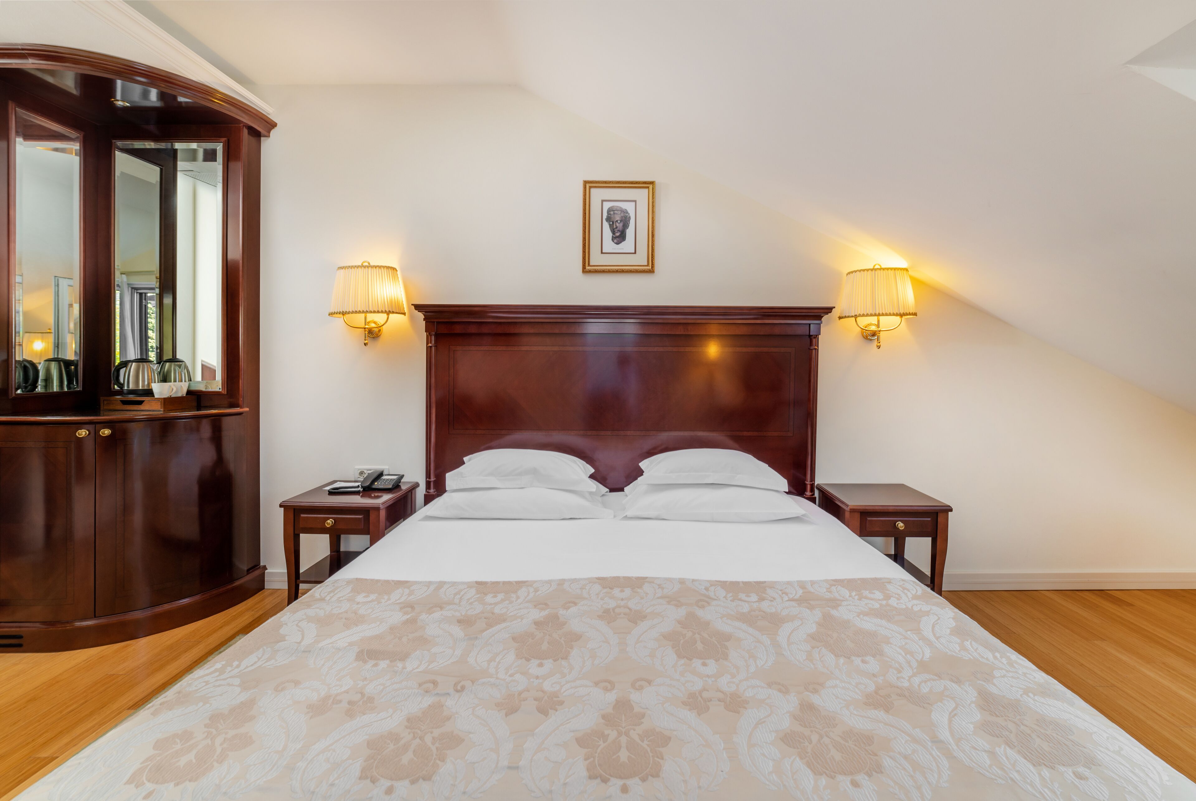 Ein ordentlich eingerichtetes Schlafzimmer mit einem großen Bett, zwei Nachttischen, einem Kleiderschrank und zwei Wandleuchten.