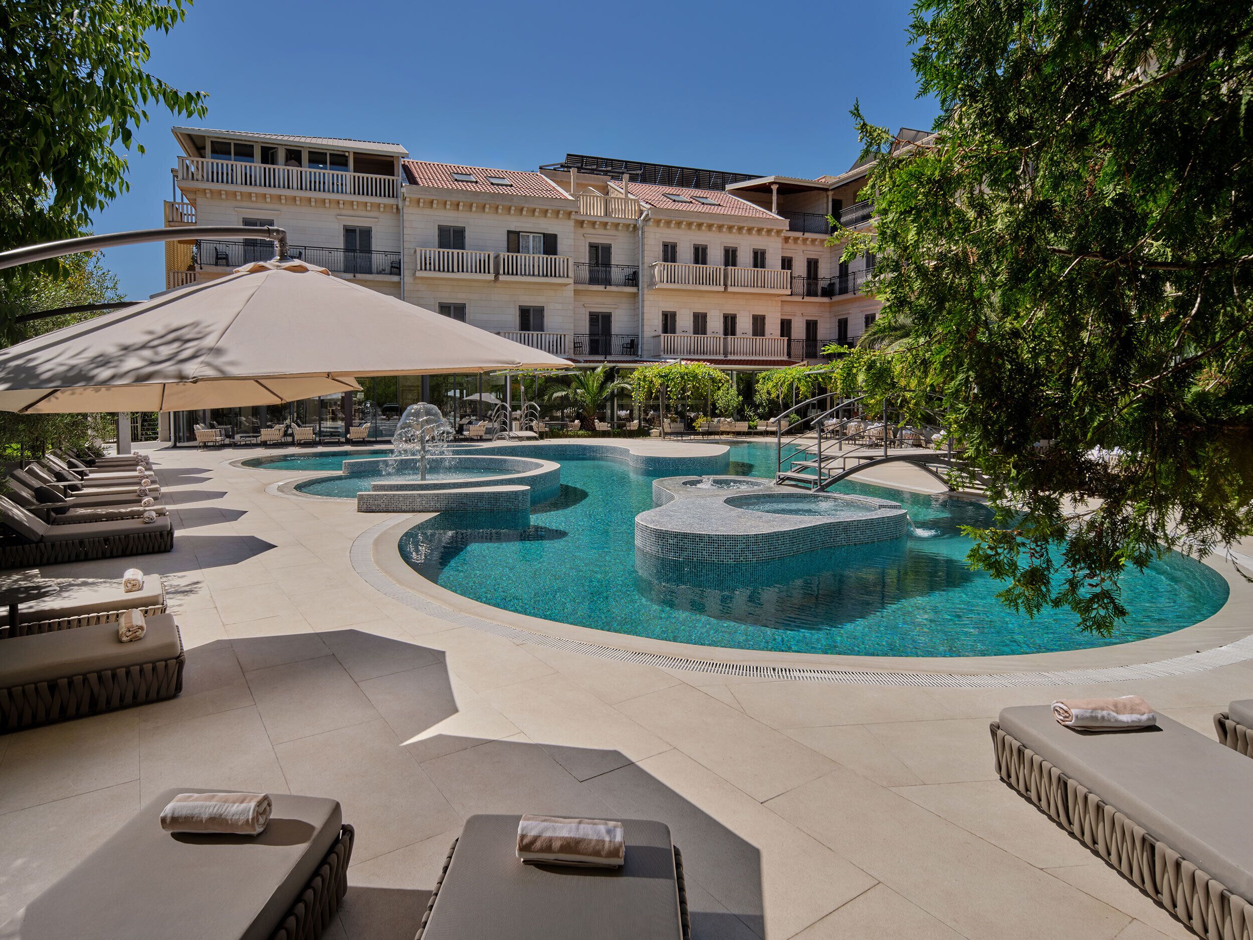 Un espace piscine doté de chaises longues et de parasols, entouré d’un bâtiment avec des balcons.
