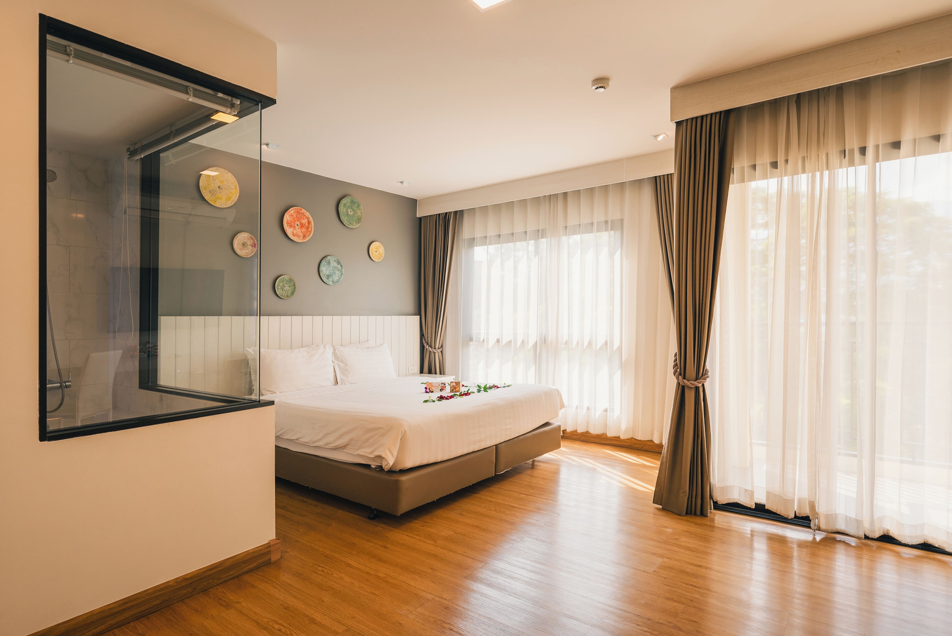 A modern bedroom with a large bed, a glass shower enclosure, and a view of the outdoors through sheer curtains.